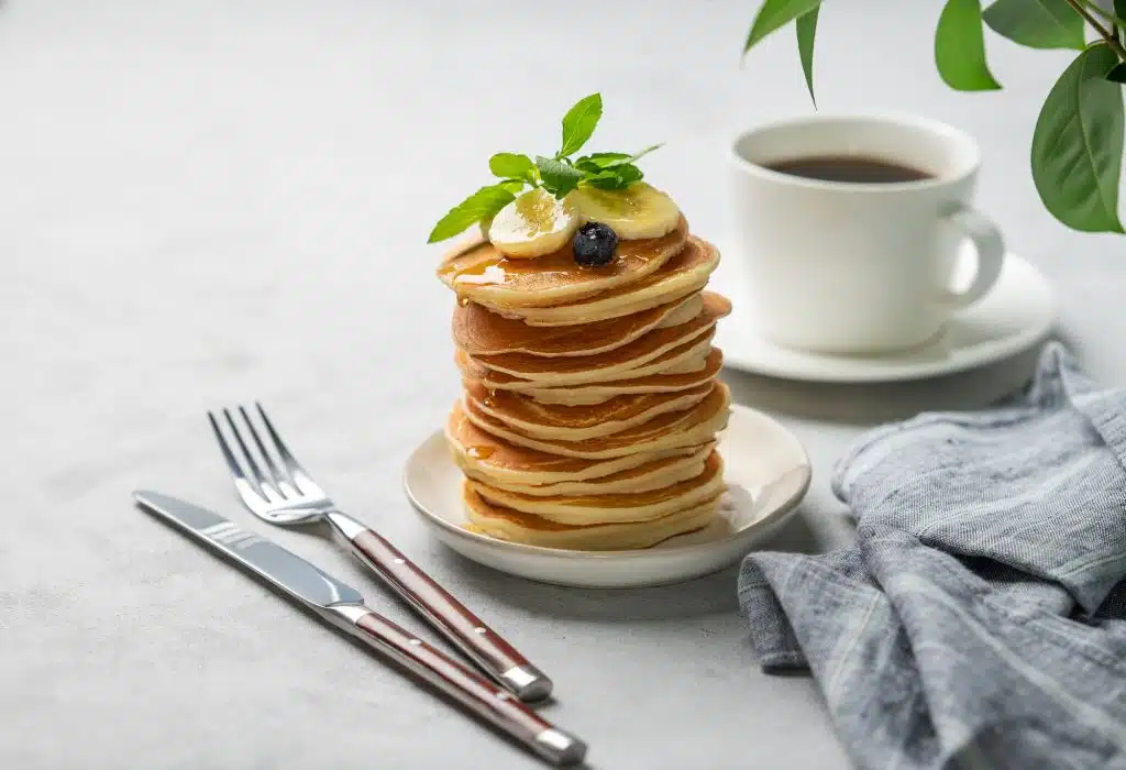 A stack of oat banana pancakes with fresh fruit slices, berries and honey on a light background